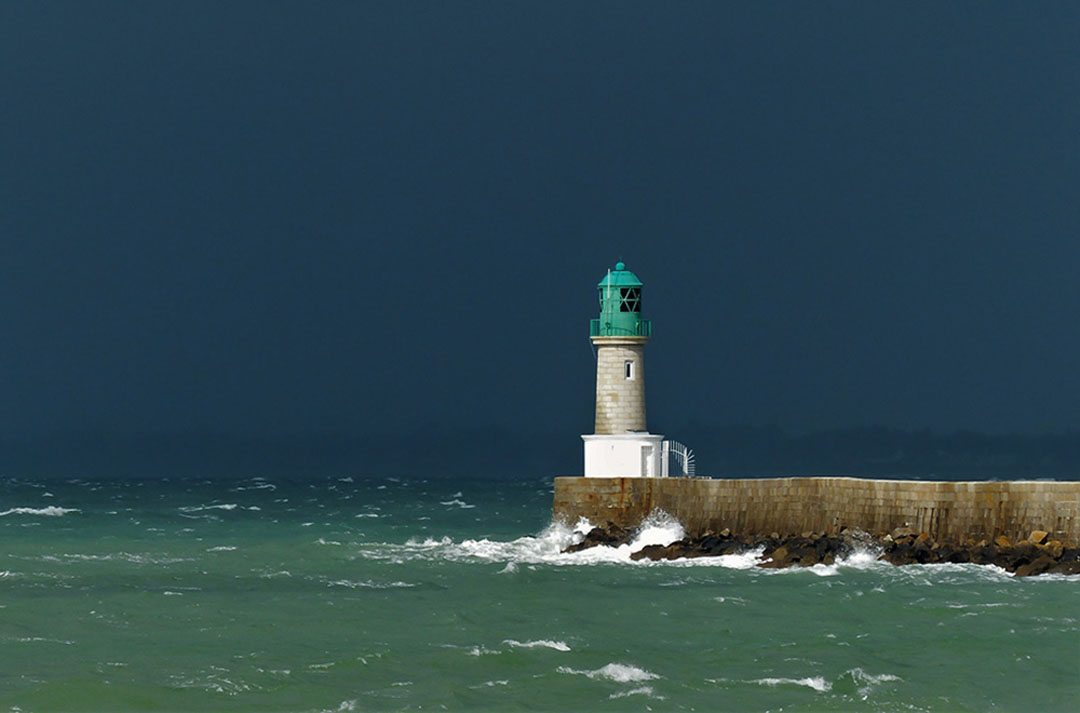 Photo d'un phare au bout d'une jetée entourée d'une mer agitée et d'un ciel chargé - référence
